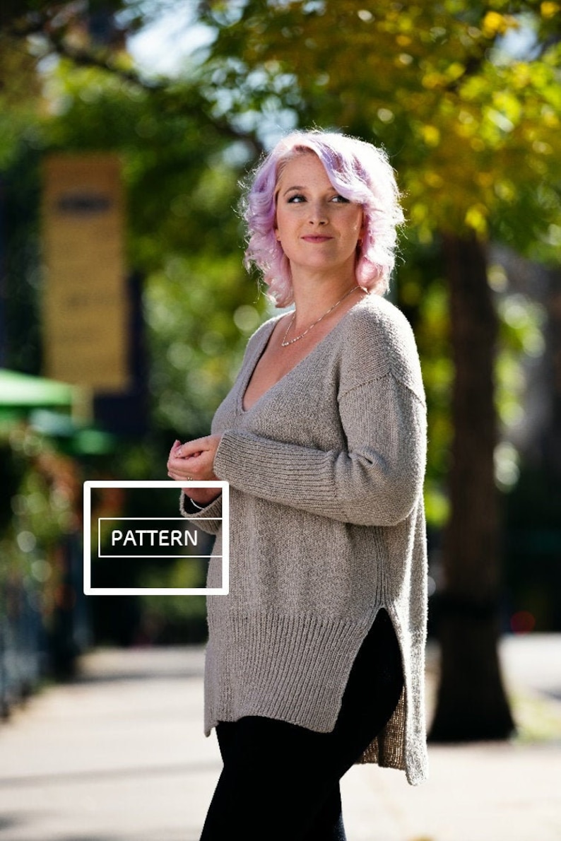 May include: A woman with purple hair is wearing a light gray knitted sweater with a side slit. The sweater has a v-neck and is loose fitting. The text "PATTERN" is visible on the sweater.
