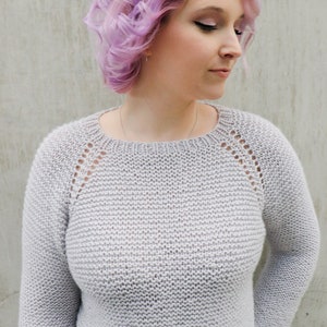 May include: A light gray knitted sweater with a round neckline and long sleeves. The sweater has a delicate lace pattern on the shoulders and a subtle texture throughout.