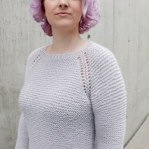 May include: A light gray knitted sweater with a round neckline and long sleeves. The sweater has a delicate openwork pattern on the shoulders and sleeves.