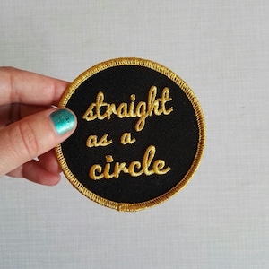 May include: A black circular patch with a gold embroidered border and the text "straight as a circle" in gold.