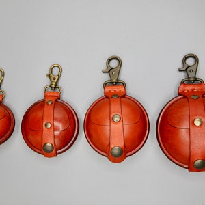 May include: Four brown leather coin purses with brass clasps and straps. The purses are different sizes and are arranged in a row from smallest to largest.