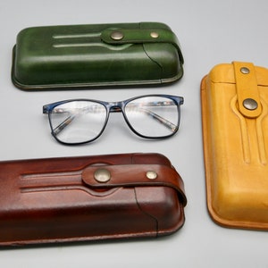 May include: Three leather eyeglass cases in different colors: green, brown, and yellow. The cases have a flap closure with a button. The cases are lined with soft fabric to protect glasses.