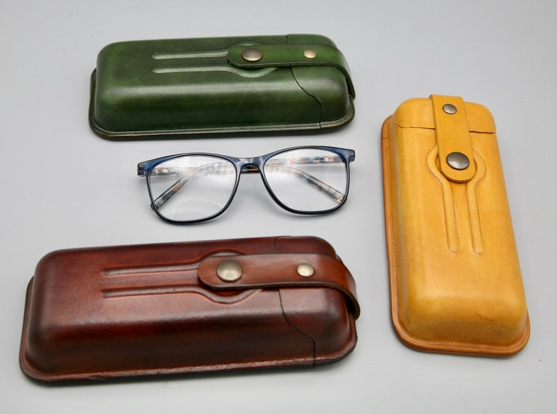 May include: Three leather eyeglass cases in different colors: green, brown, and yellow. The cases have a flap closure with a button. The cases are lined with soft fabric to protect glasses.