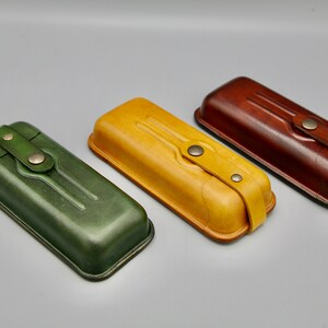 May include: Three leather cases in green, yellow, and brown. Each case has a flap with a strap and a metal button closure.