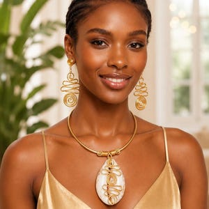 Peut inclure: Un ensemble de bijoux en fil métallique doré composé d'un collier ras-de-cou et de boucles d'oreilles pendantes assorties. Le collier présente un grand pendentif en coquillage blanc en forme de goutte, entouré de fil doré torsadé.
