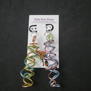 May include: A pair of handmade earrings with a spiral design. The earrings are made of wire and are available in a variety of colors, including gold, green, pink, and blue. The earrings are shown on a white card with the text "Softly Sister Designs Unique Hand Crafted Jewelry www.etsy.com/shop/softlysisterdesigns".