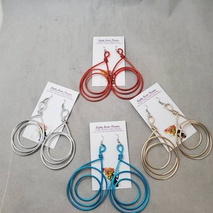 May include: Four pairs of dangle earrings with a triple-loop design. The earrings are made of wire and come in silver, gold, red, and blue.