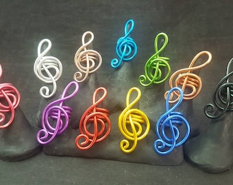 Peut inclure: Un ensemble de dix bagues en fil de fer de couleur en forme de clés de sol. Les bagues sont exposées sur de petits supports noirs.