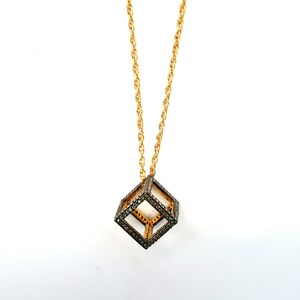 May include: A gold chain necklace with a black diamond cube pendant. The cube is made of a wire frame with black diamonds set into the frame.