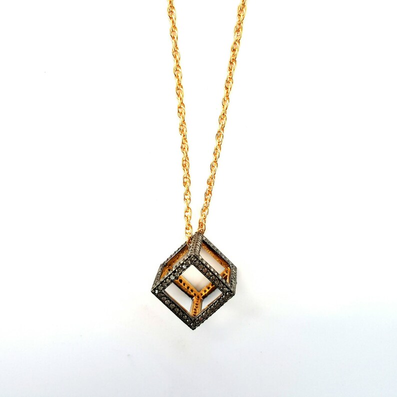 May include: A gold chain necklace with a black diamond cube pendant. The cube is made of a wire frame with black diamonds set into the frame.
