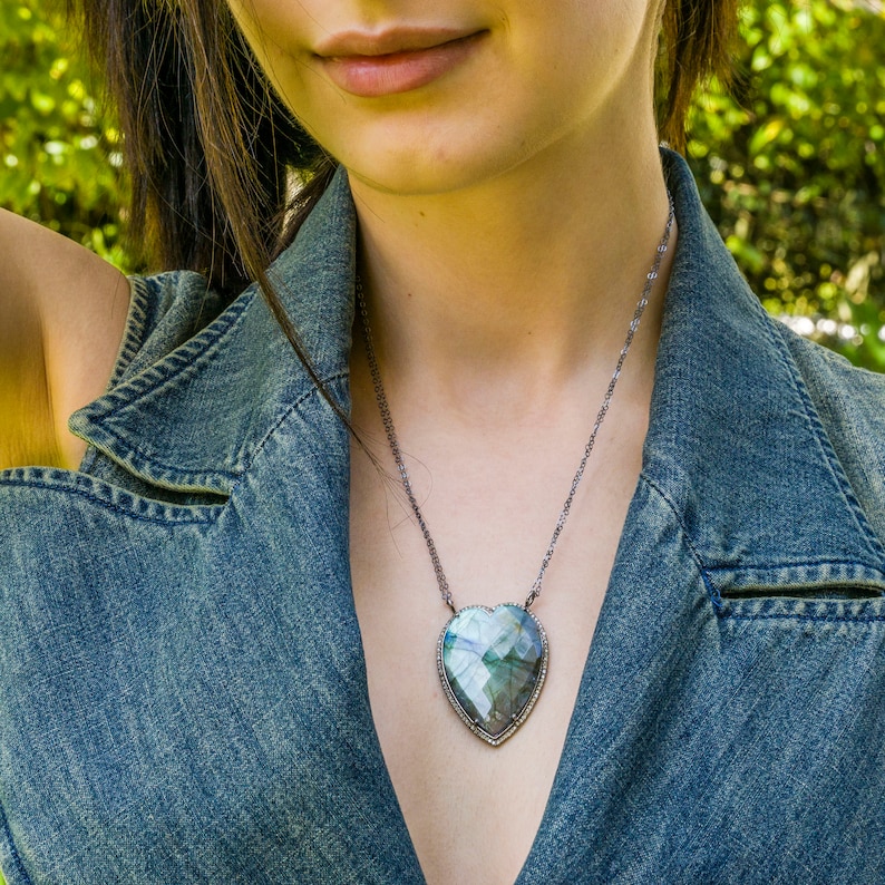 Puede incluir: Un collar de cadena de plata con un gran colgante de labradorita facetado en forma de coraz&oacute;n. El colgante est&aacute; rodeado por un borde de peque&ntilde;as piedras preciosas transparentes.