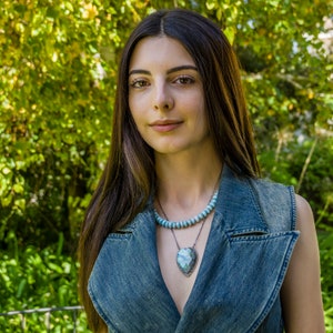 Puede incluir: Una mujer con el pelo largo y casta&ntilde;o lleva un chaleco vaquero y un collar con un gran colgante de coraz&oacute;n turquesa.