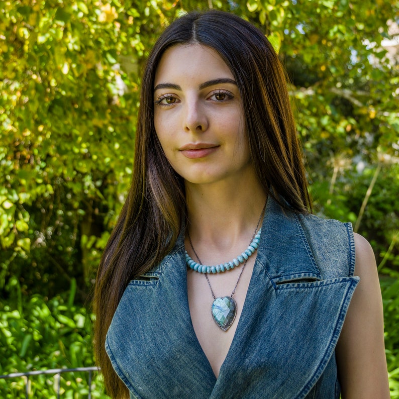 Puede incluir: Una mujer con el pelo largo y casta&ntilde;o lleva un chaleco vaquero y un collar con un gran colgante de coraz&oacute;n turquesa.