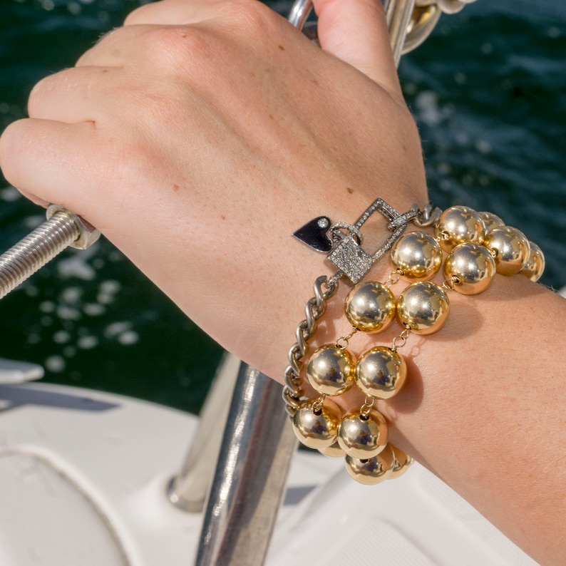 May include: A gold bracelet with multiple strands of large, round beads and a small charm with a heart and a diamond-encrusted padlock.