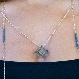 May include: A gold chain necklace with a geometric pendant featuring a cube shape with black diamond accents.