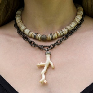 May include: A layered necklace with a silver chain and a white coral pendant. The top layer is a white and brown beaded necklace.