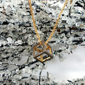 May include: A gold chain necklace with a diamond-encrusted cube pendant. The cube is made of gold and has a geometric design. The necklace is photographed against a sparkly background.