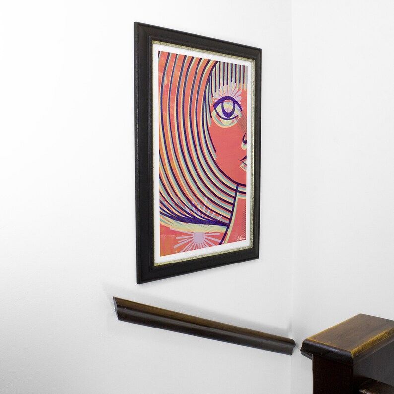 May include: A framed abstract art print of a woman's face with colorful stripes and a single eye. The background is a light orange color.
