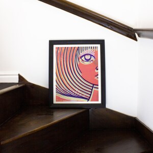 May include: A framed print of a colorful abstract portrait of a person with a large eye and a pink face. The background is a mix of yellow, blue, and green stripes.