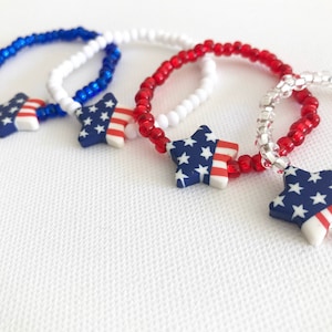 May include: Three beaded bracelets with star-shaped charms. The stars are decorated with the American flag colors of red, white, and blue.