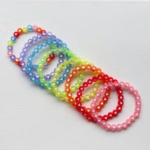 Könnte beinhalten: Ein Set aus acht regenbogenfarbenen Armbändern aus kleinen herzförmigen Perlen. Die Armbänder sind spiralförmig angeordnet.