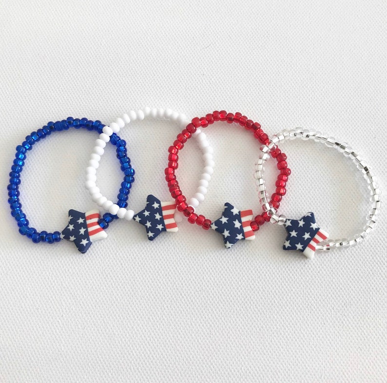 May include: Three beaded bracelets with star-shaped charms. Each bracelet is made with white, red, and blue beads, resembling the colors of the American flag. The star charms are decorated with the American flag pattern.