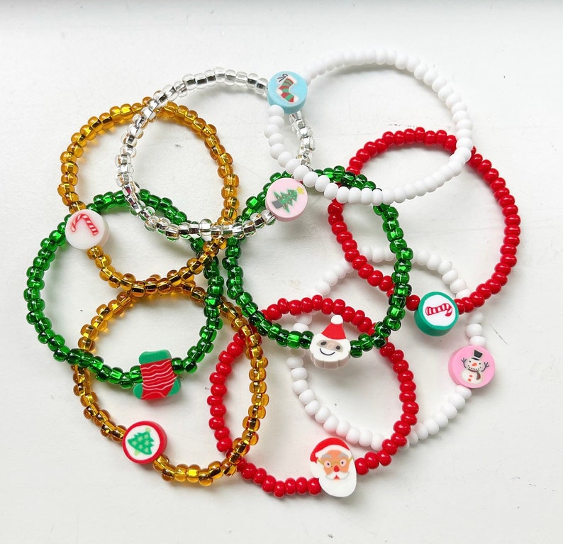 Puede incluir: Un conjunto de pulseras de cuentas coloridas con dijes de tem&aacute;tica navide&ntilde;a. Los dijes incluyen un mu&ntilde;eco de nieve, una media, un bast&oacute;n de caramelo, un &aacute;rbol de Navidad y Santa Claus.