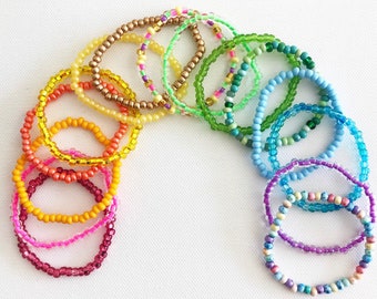 May include: A set of colorful beaded bracelets in various shades of green, blue, yellow, orange, and pink. The bracelets are made of small, round beads and are arranged in a rainbow pattern.