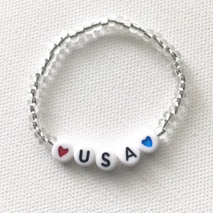 May include: A white beaded bracelet with the letters "USA" and red and blue hearts.