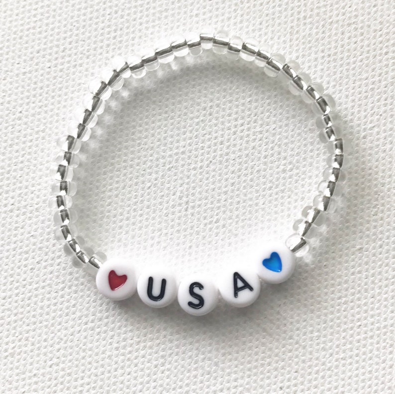 May include: A white beaded bracelet with the letters "USA" and red and blue hearts.