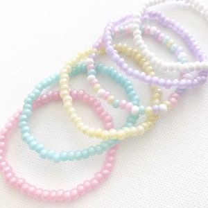May include: A set of six pastel-colored beaded bracelets. The bracelets are made of small, round beads in shades of pink, blue, yellow, and purple.