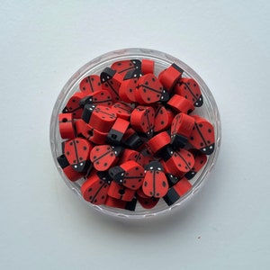 K&ouml;nnte beinhalten: Ein durchsichtiger Plastikbeh&auml;lter gef&uuml;llt mit roten und schwarzen Marienk&auml;fer-Perlen. Die Perlen sind aus Polymer Clay und haben eine gl&auml;nzende Oberfl&auml;che.