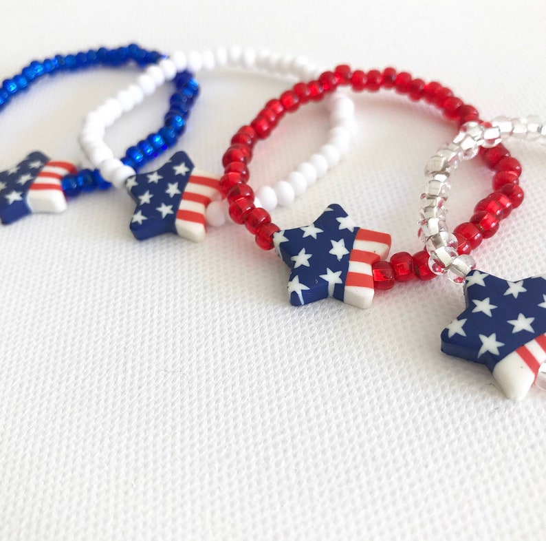 May include: Three beaded bracelets with star-shaped charms. The stars are decorated with the American flag colors of red, white, and blue.