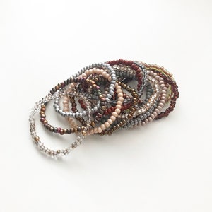 May include: A stack of beaded bracelets in various shades of brown, silver, and beige.