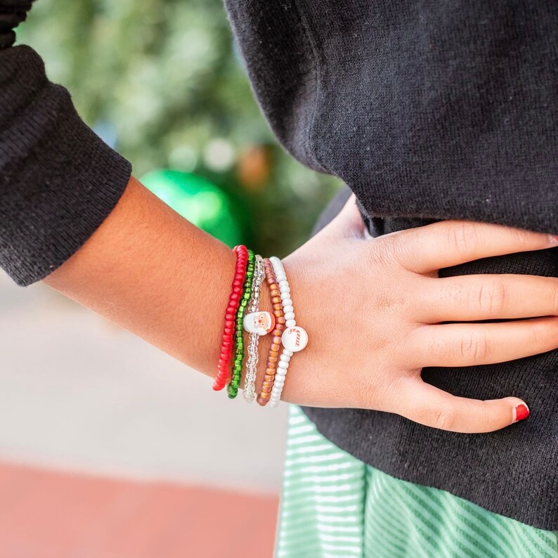 Puede incluir: Una persona lleva un su&eacute;ter negro y una falda a rayas blancas y verdes. Lleva varias pulseras en la mu&ntilde;eca, incluyendo una pulsera de cuentas rojas, una pulsera de cuentas verdes, una pulsera de cadena plateada y una pulsera de cuentas blancas con un dije.
