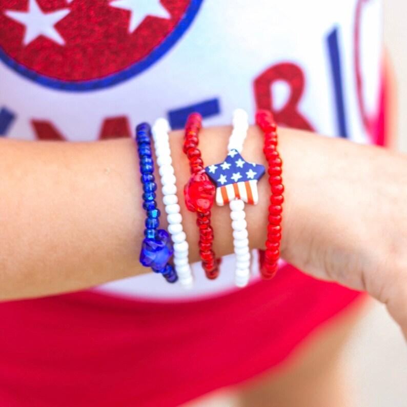 May include: A stack of red, white, and blue beaded bracelets with a star-shaped charm featuring the American flag.