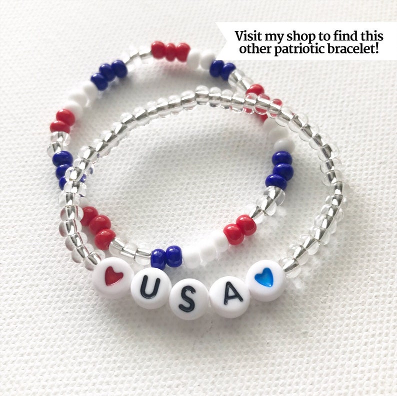 May include: A red, white, and blue beaded bracelet with the word "USA" spelled out in white beads with a red heart bead on one end and a blue heart bead on the other end.