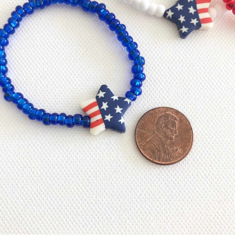 May include: A blue beaded bracelet with a star-shaped charm featuring the American flag design. The charm is about the size of a US penny.