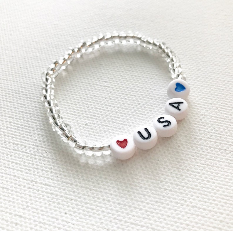 May include: A white beaded bracelet with the letters "USA" and two hearts, one red and one blue.