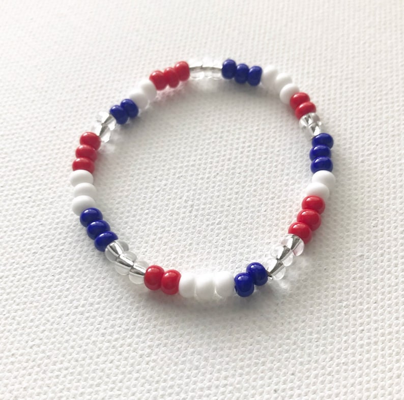 May include: A red, white, and blue beaded bracelet. The bracelet is made with small, round beads and has a clear elastic string.