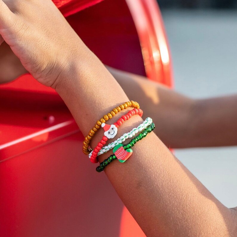 Puede incluir: Una mu&ntilde;eca con cuatro pulseras de cuentas de colores con dijes navide&ntilde;os. Las pulseras son rojas, blancas, verdes y doradas.