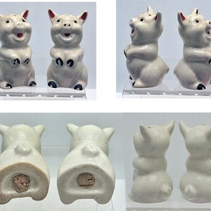 May include: A pair of vintage ceramic pig salt and pepper shakers. The pigs are off-white with black accents on their hooves and ears. They have smiling faces and are standing upright.