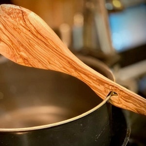 May include: A wooden kitchen utensil with a natural wood grain pattern. The utensil is resting on the edge of a black pot.