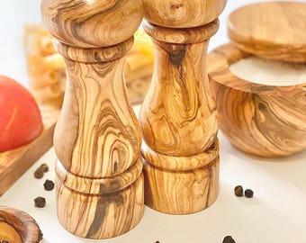 May include: A set of two wooden salt and pepper shakers with a natural wood grain finish. The shakers are made of olive wood and have a classic design.