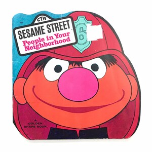 May include: A Sesame Street children's book featuring Big Bird dressed as a firefighter. The book cover is red, orange, and blue with the title "Sesame Street People in Your Neighborhood".