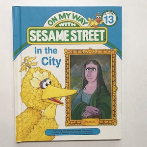 May include: A yellow Big Bird Sesame Street character looks at a painting of Mona Lisa in a book titled "On My Way With Sesame Street: In the City". The book is volume 13.