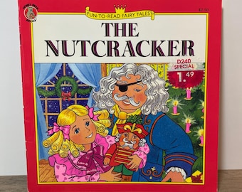 May include: A vintage children's book titled "The Nutcracker" with a red cover. The cover features illustrations of characters from the story, including a girl, a man with an eye patch, and a nutcracker doll. The book is part of the "Fun-To-Read Fairy Tales" series.