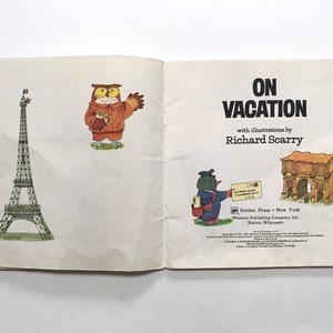 May include: An open book with the title "On Vacation" by Richard Scarry. The book features illustrations of an owl, a penguin, the Eiffel Tower, and the Arch of Constantine.