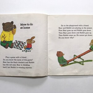 May include: A children's book illustration showing a brown bear and a rabbit playing checkers and a brown bear and a rabbit playing on a seesaw. The text on the page reads "More to do at home" and "Go to the playground with a friend. Bear and Rabbit are playing on the seesaw. First Bear goes up and Rabbit goes down. Then Bear goes down and Rabbit goes up. Then Rabbit stays up. He cannot get down. Do you know why?" and "Play a game with a friend. Do you know the name of this game? Bear has the black checkers and Rabbit has the red ones. Bear is thinking hard, but Rabbit is winning anyway."