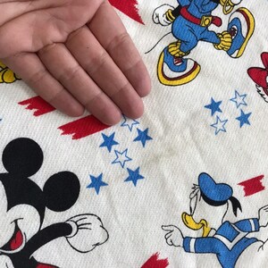 May include: White fabric with a red, white and blue pattern featuring Mickey Mouse, Donald Duck and Minnie Mouse. The fabric has a red, white and blue star pattern.